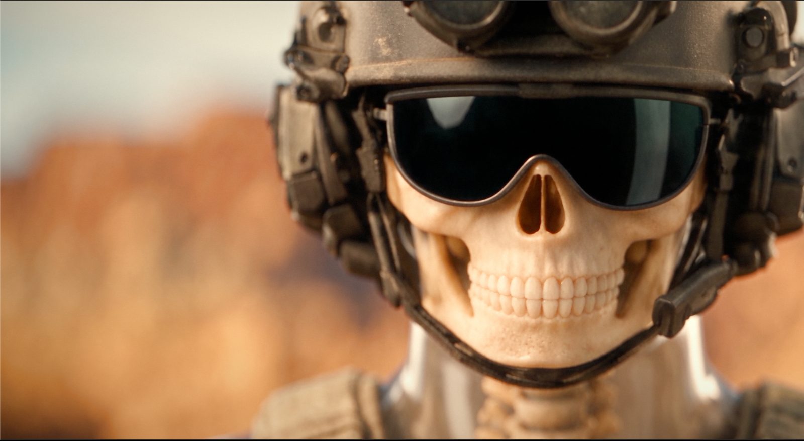 Sgt. Joe, Nahaufnahme: gläserner Totenkopf-Soldat mit Helm und Schutzbrille vor Wüstenunschärfe